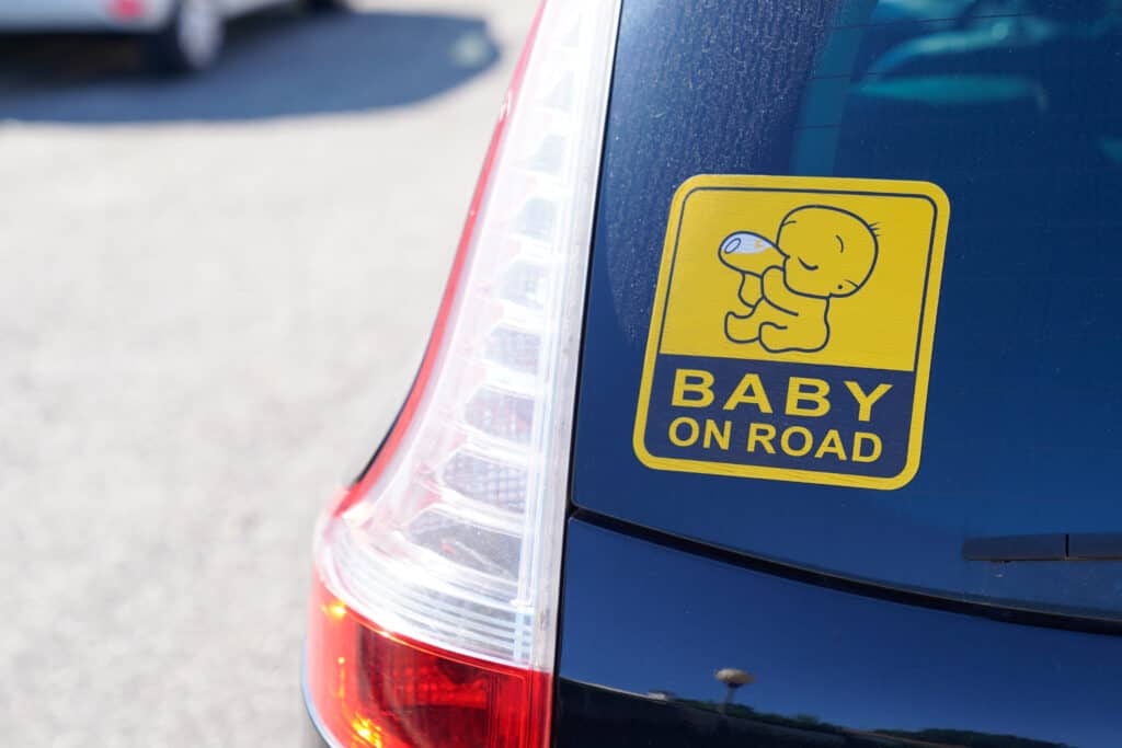 סטיקר לאוטו בצבע צהוב המודבק על רכב כחול ועליו הכיתוב ״תינוק באוטו״ באנגלית.